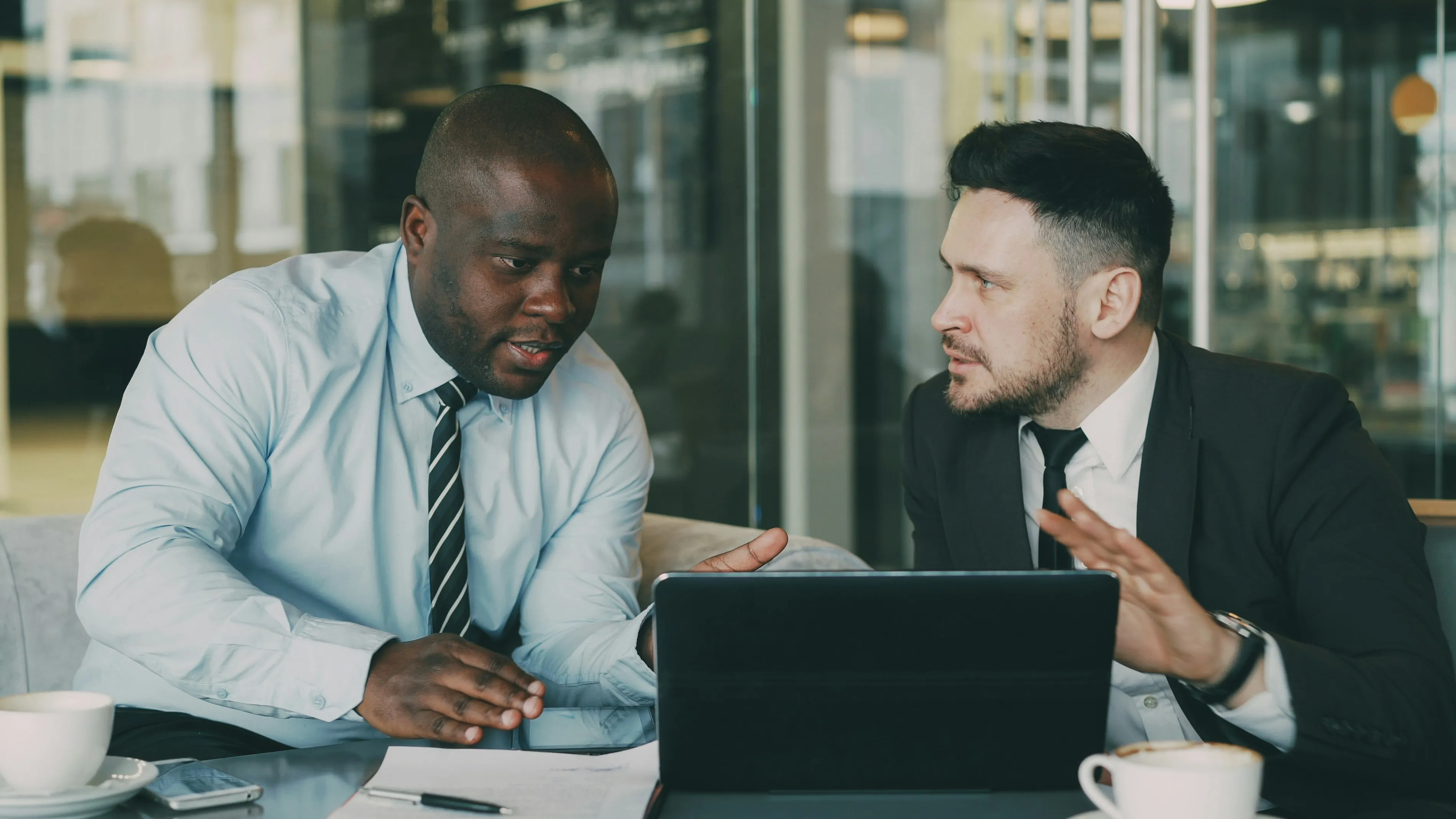 Two businessmen collaborating over a tablet and laptop