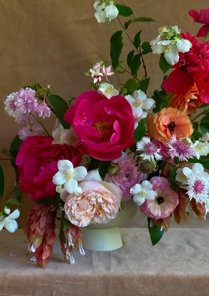 Arreglo floral vibrante con peonías, ranúnculos y flores silvestres en tonos rosados y naranjas, composición artística y expresiva.