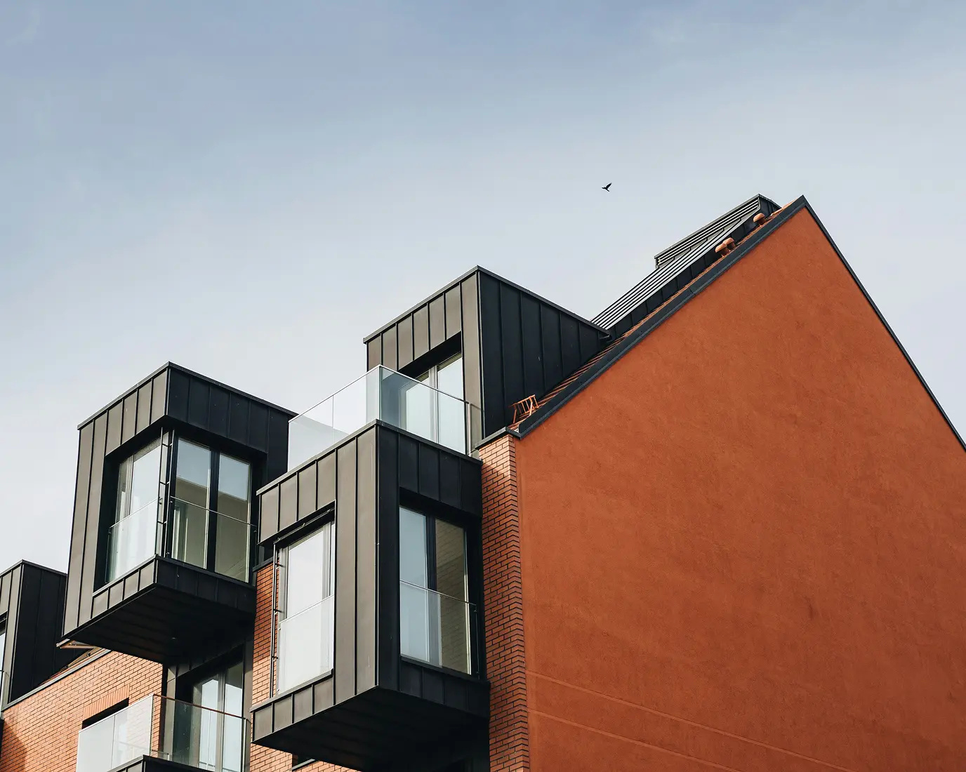 Modern building exterior with black-framed, glass-enclosed balconies. The red brick facade contrasts with a clear sky, evoking a sleek, contemporary feel.