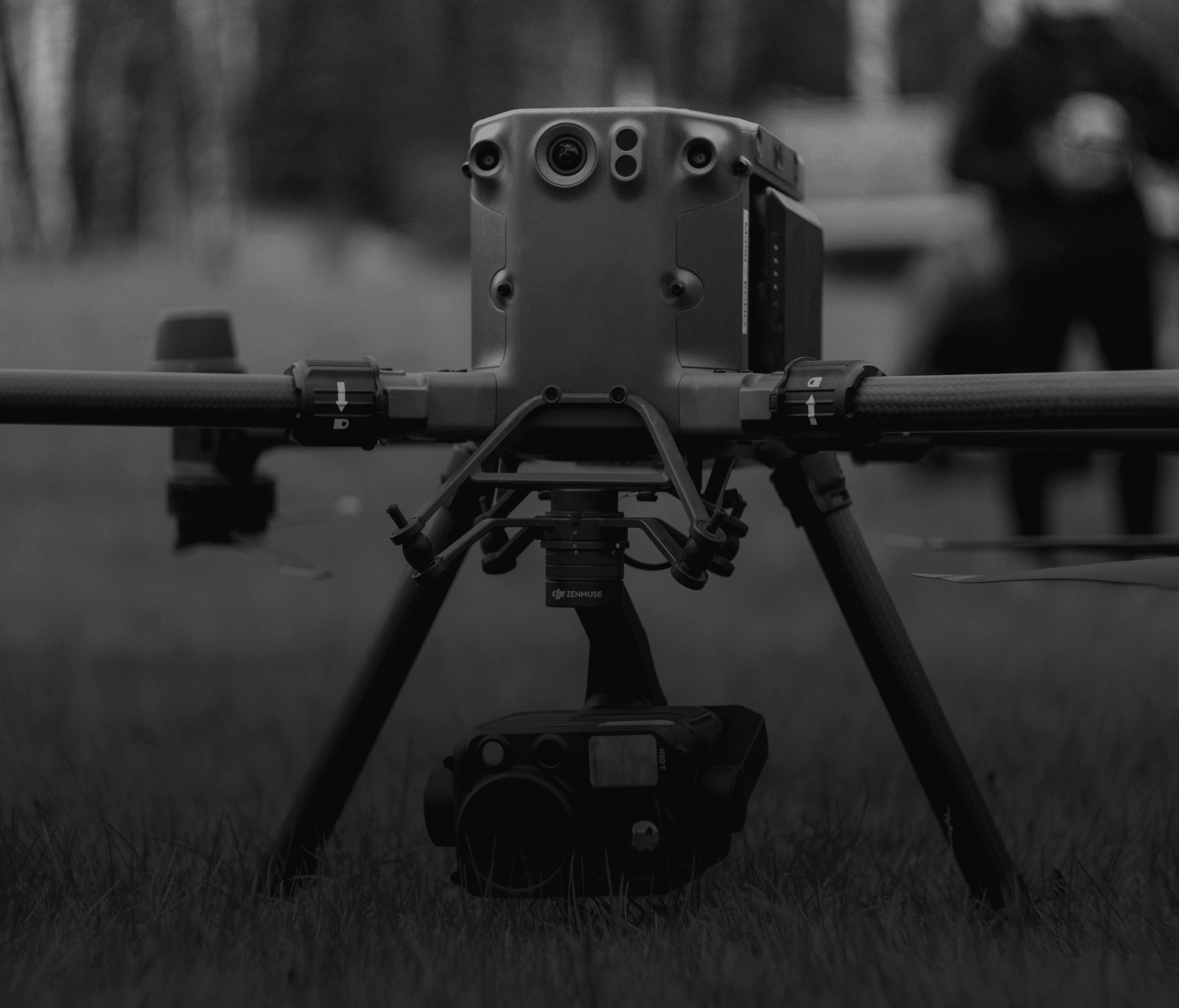 A black quadcopter drone with four propellers is equipped with a camera mounted underneath, designed for aerial photography and surveillance.