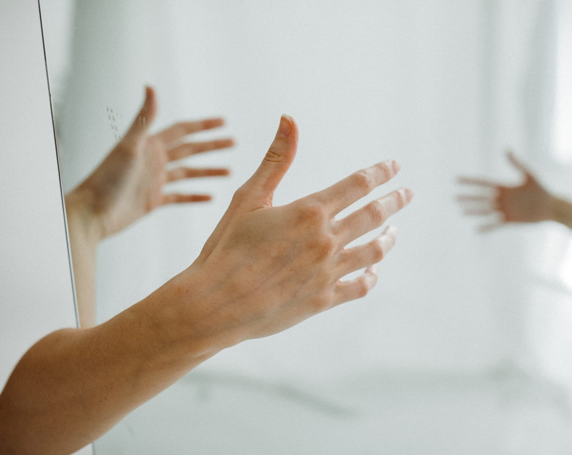 Hands reaching toward a mirror in soft natural light at Revelator Studio in Shreveport, creating a minimalist and artistic reflection.