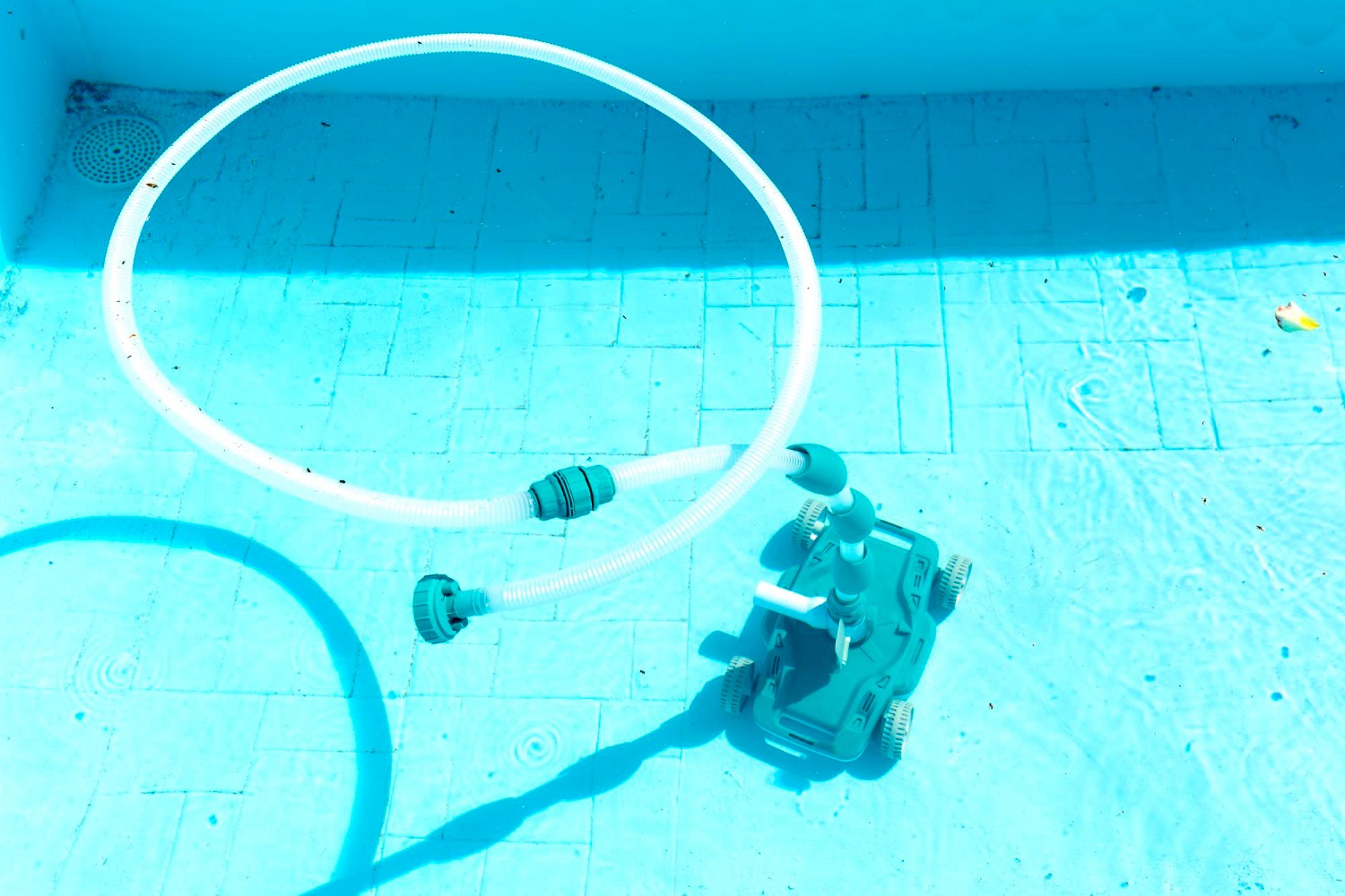 Automatic pool cleaner with a long hose operating on the floor of a light-blue residential pool.