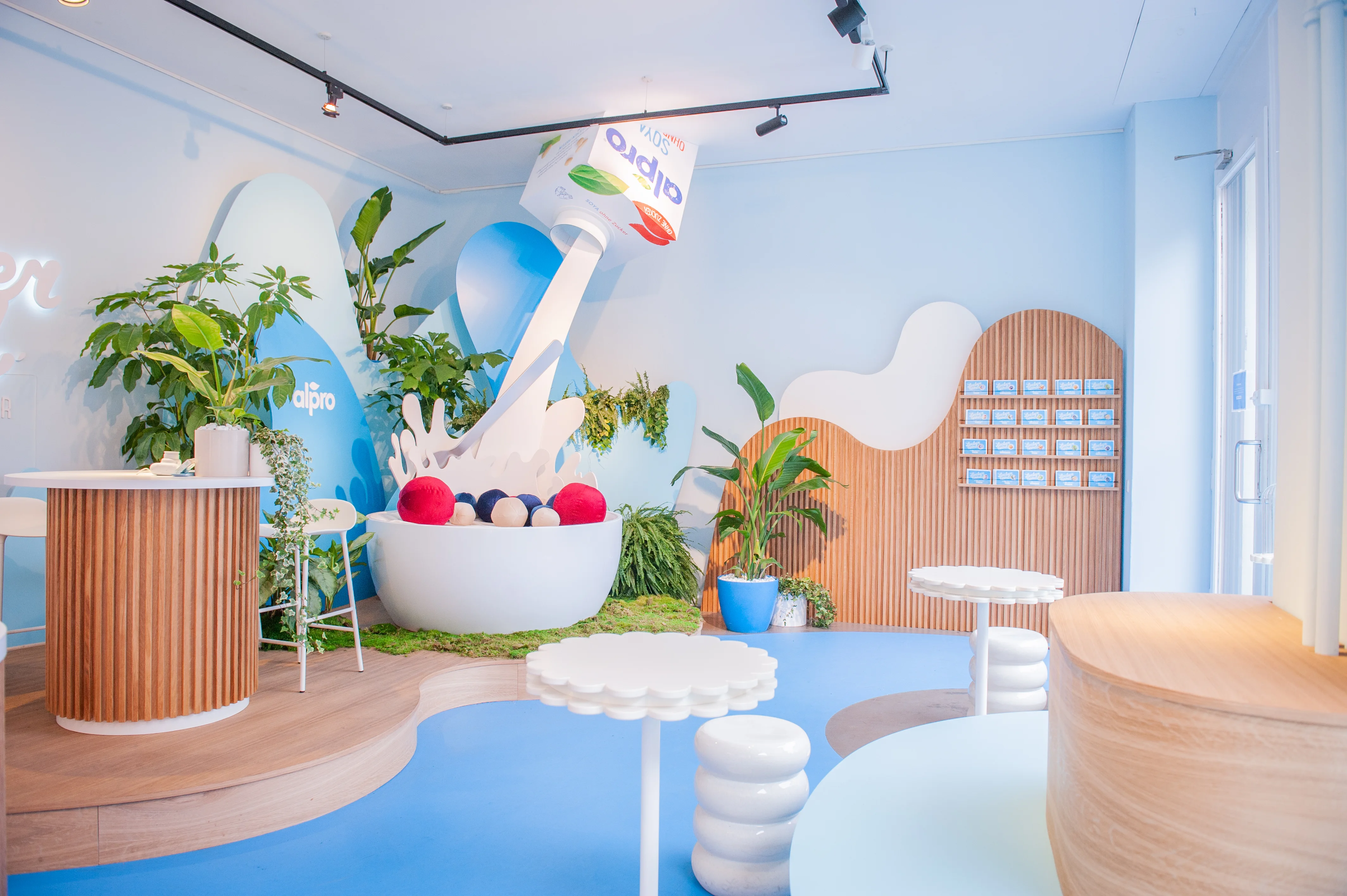Installation of a floating Alpro carton pouring into a giant bowl with colorful berry balls amid plants at the Leckerland pop-up.