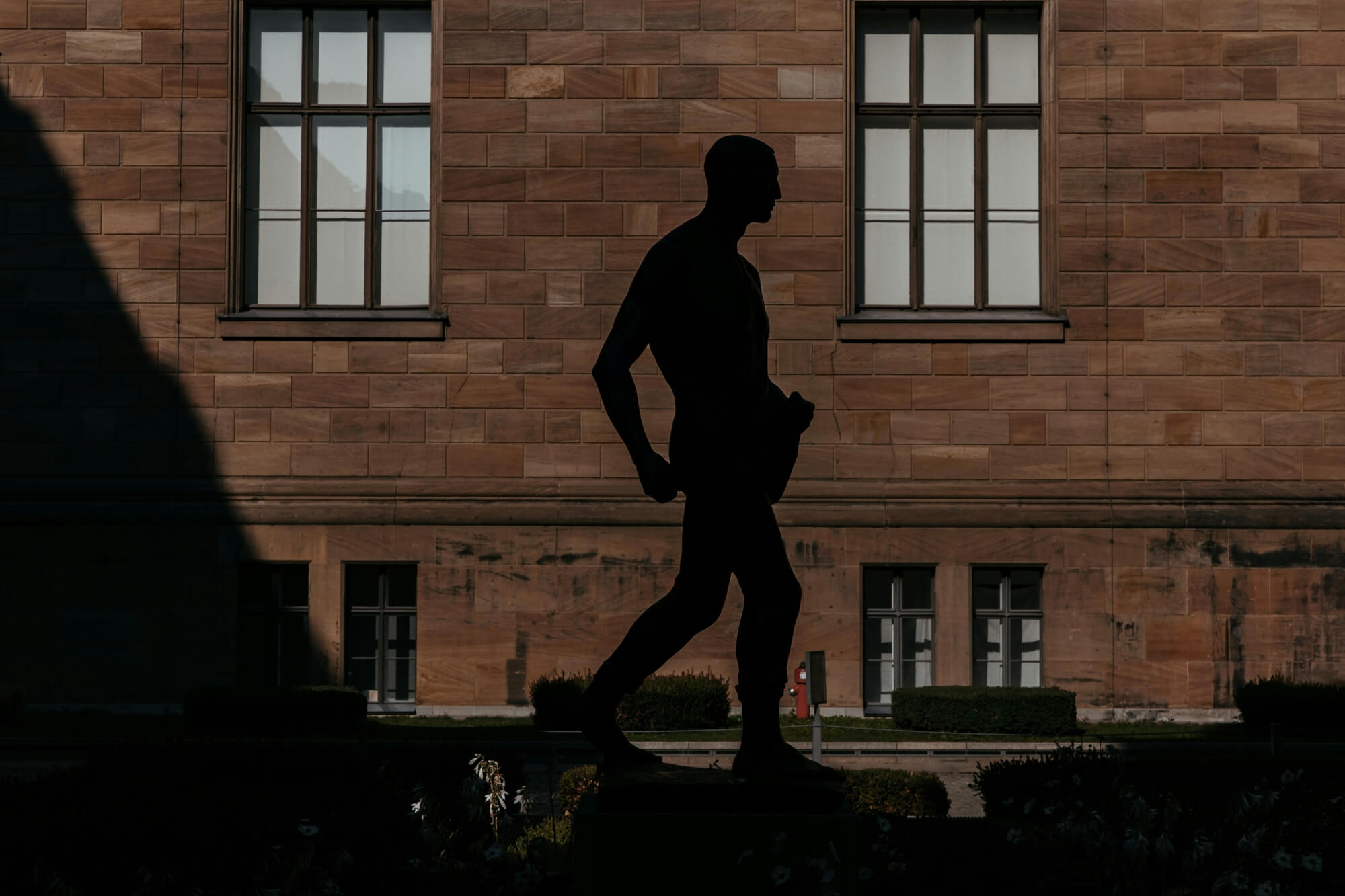 A silhouette of a statue walking against a backdrop of brick walls and windows.