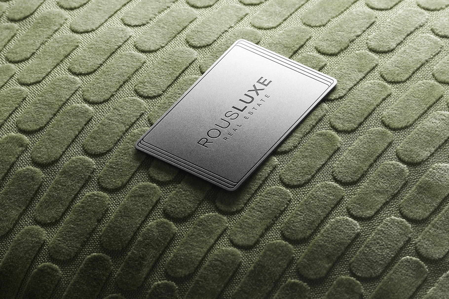 Logo mockup on a silver metal card resting on green textured fabric.