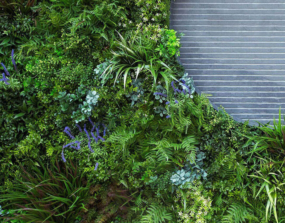 A VistaFolia Artificial Green Wall peppered with colorful VistaFolia Color Box plants, the entirety of which is arranged in a circular shape encompassing a ribbed concrete wall.