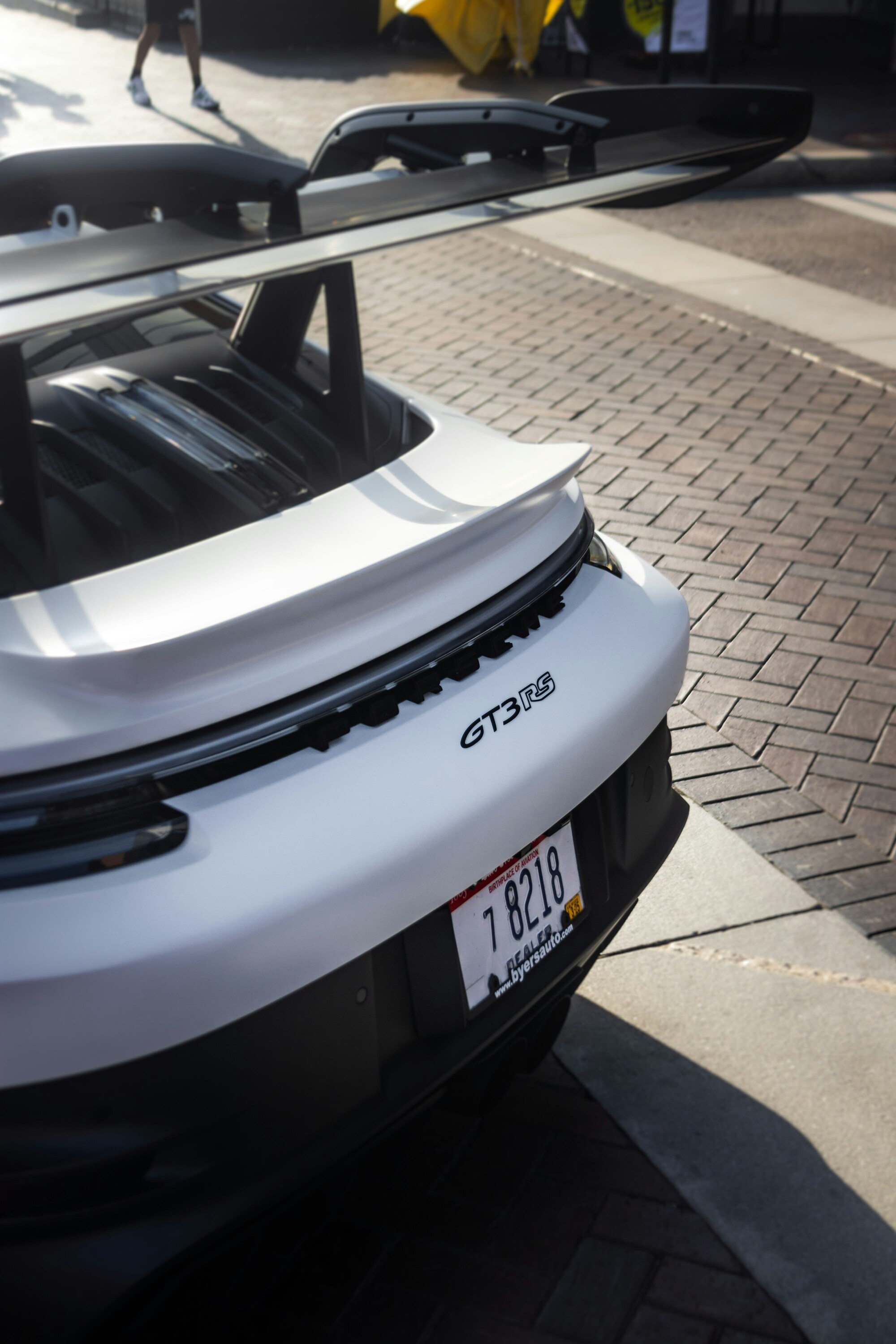 A sleek, white sports car with a prominent rear spoiler and "GT3 RS" badge is parked on a patterned brick surface, highlighting its aerodynamic design.