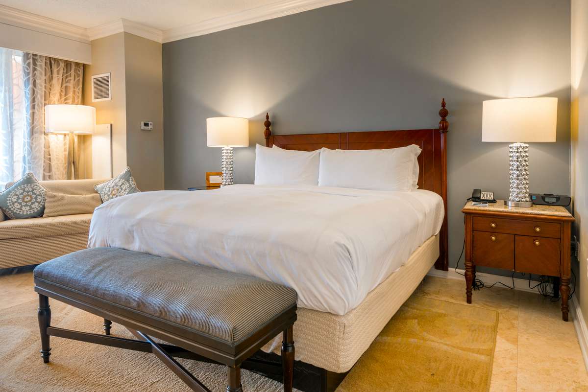 A hotel room with a large bed featuring white linens and pillows, flanked by two bedside tables with lamps.