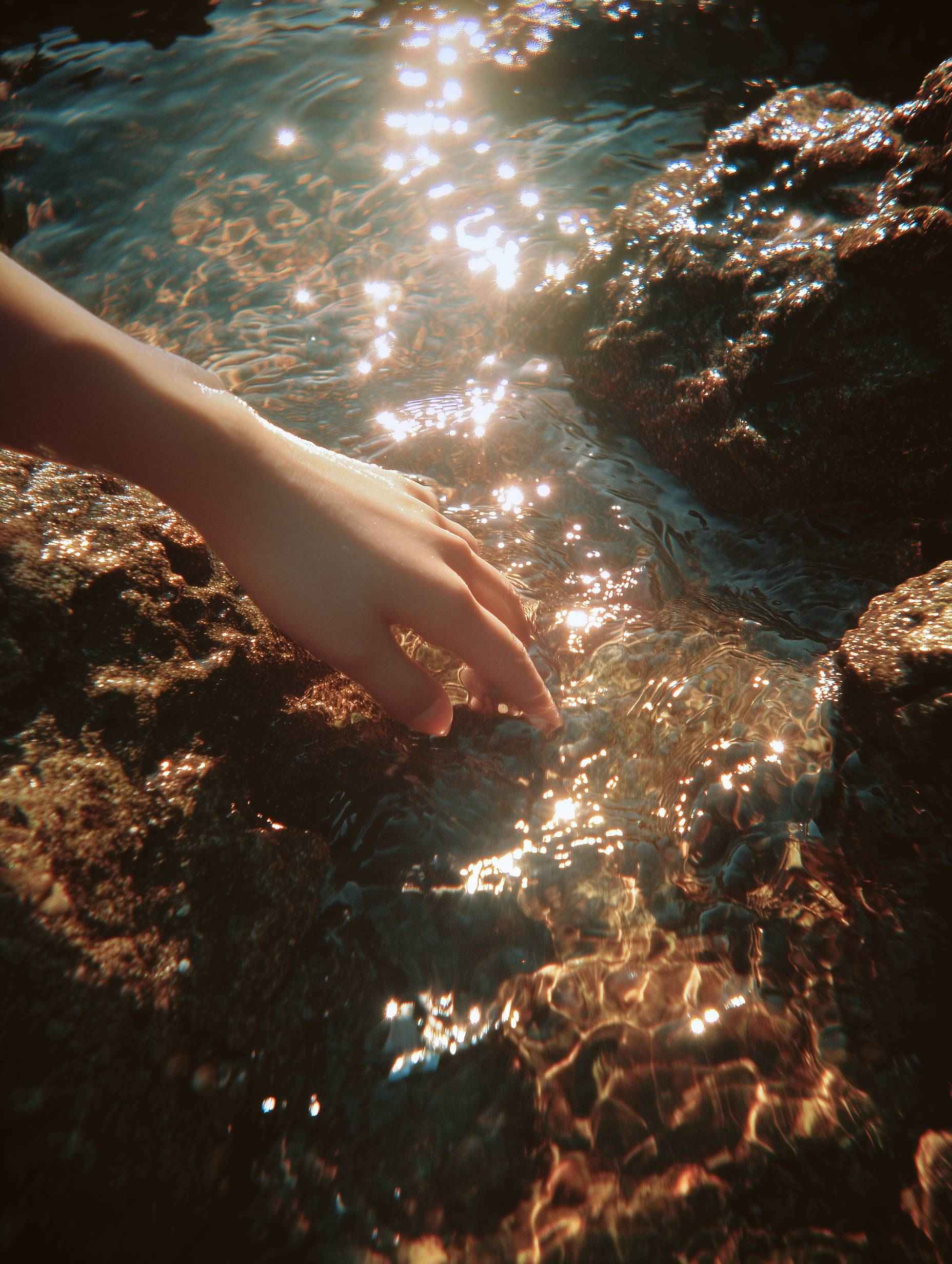 Hand reaching into luminous aquamarine water close-up