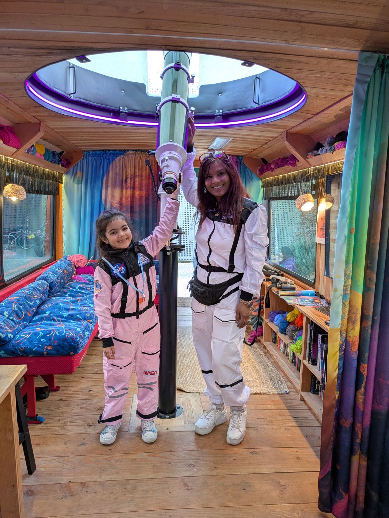 Mother and daughter in matching space suits stading with the telescope on board the Moon palace bus