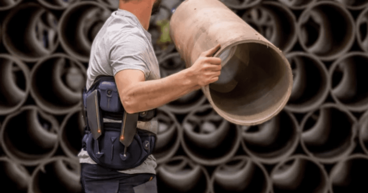 Worker wearing a lumbar support exoskeleton to lift a heavy object in an industrial environment, enhancing safety and reducing fatigue.