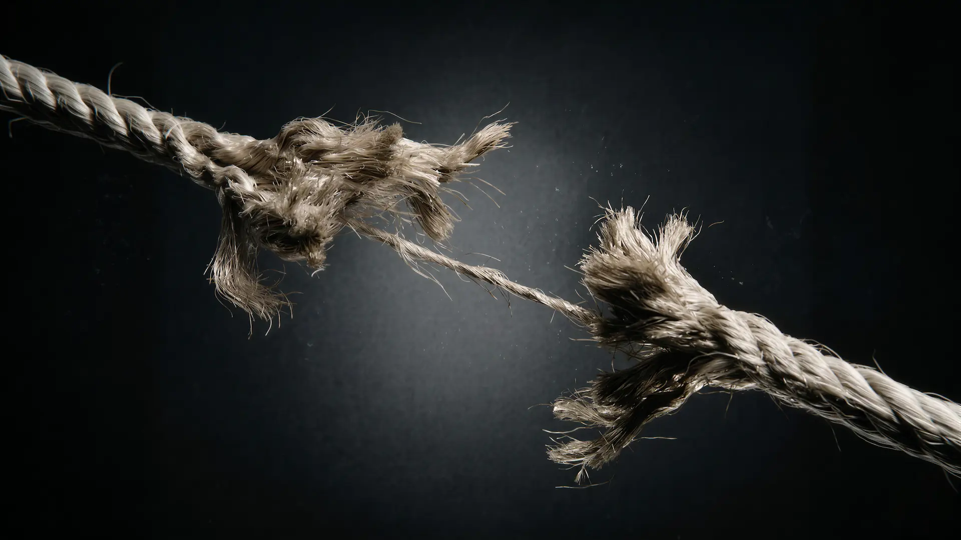Thick rope fraying under tension with fibers separating against a dark background.