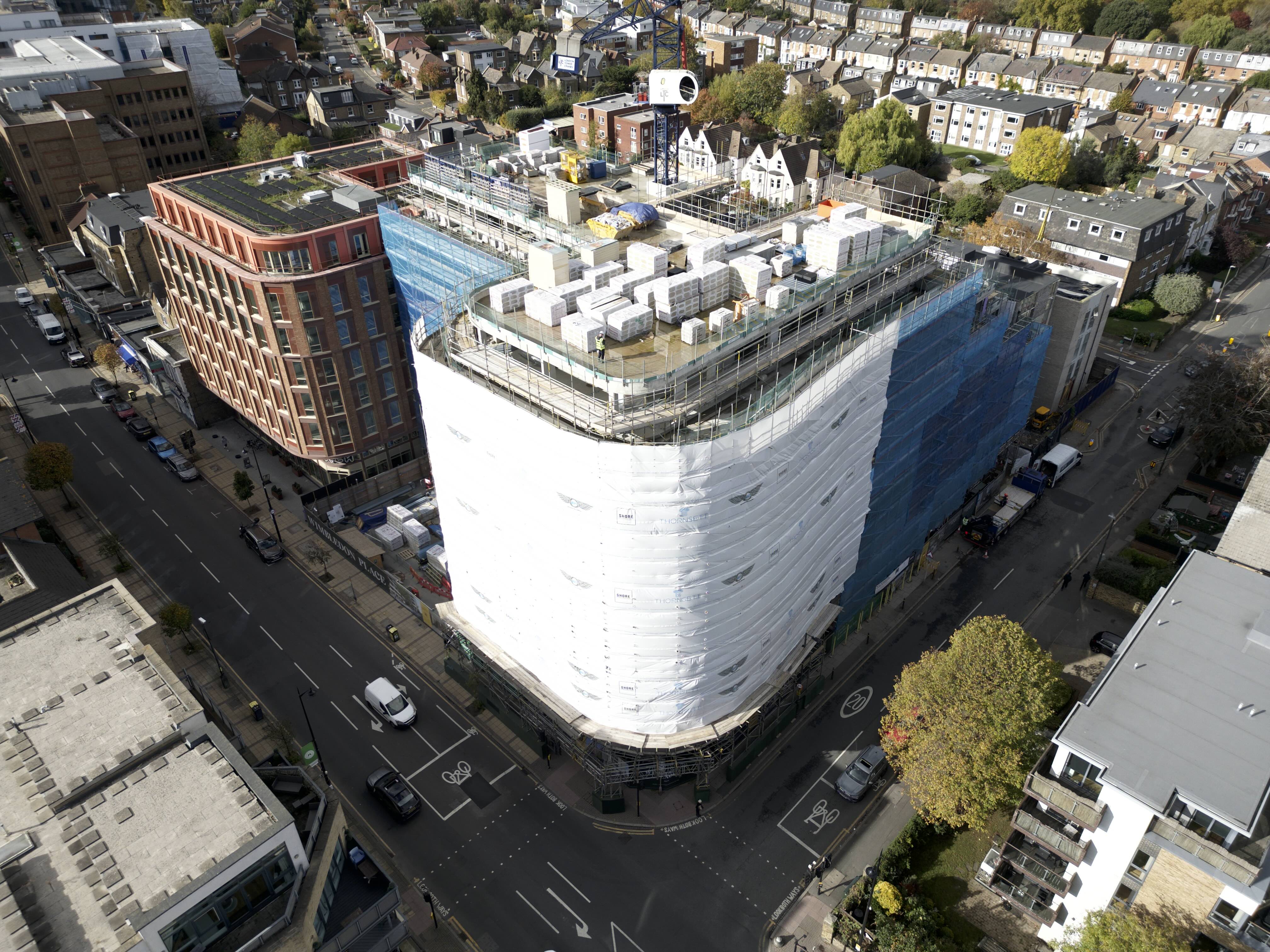A group of construction workers wearing high-visibility jackets and hard hats celebrate at a construction site with safety signs and equipment visible in the background.