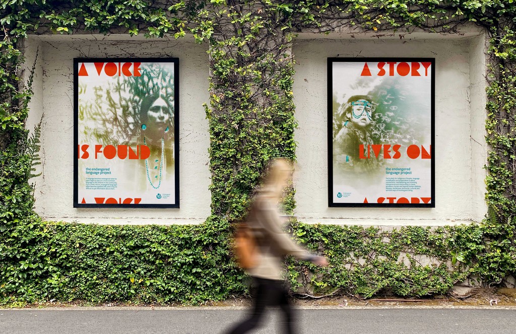 Woman walking past two large, cyanotype posters on a vine-covered wall.