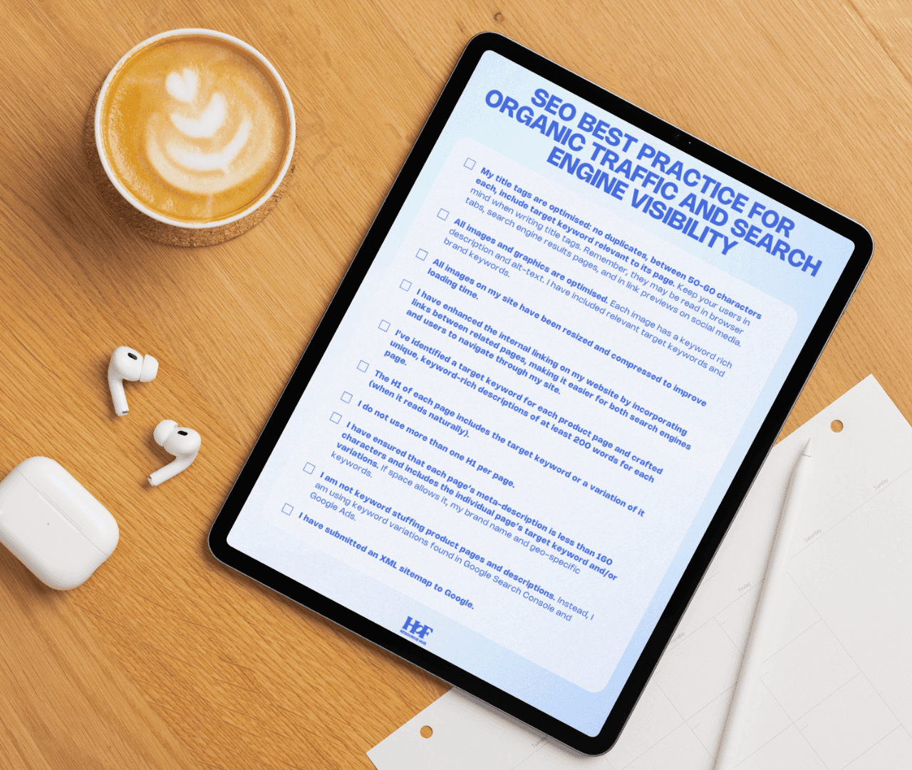 SEO Checklist on tablet laying on wooden table. Next to the tablet (L) is a cup of coffee and a case for ear pods. The ear pods are lose next to the case.