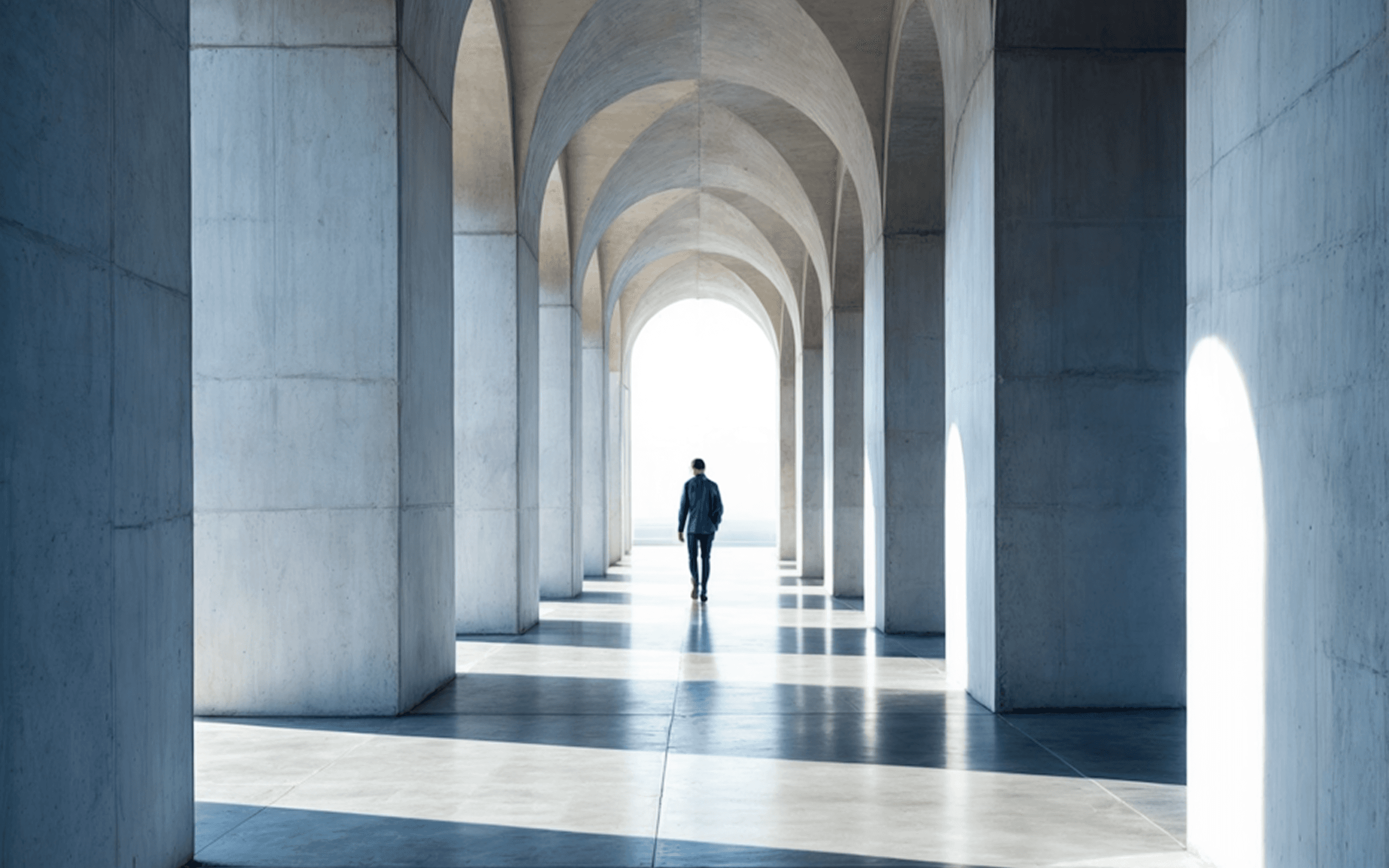 A man walks away down a long, bright hall of modern concrete arches.