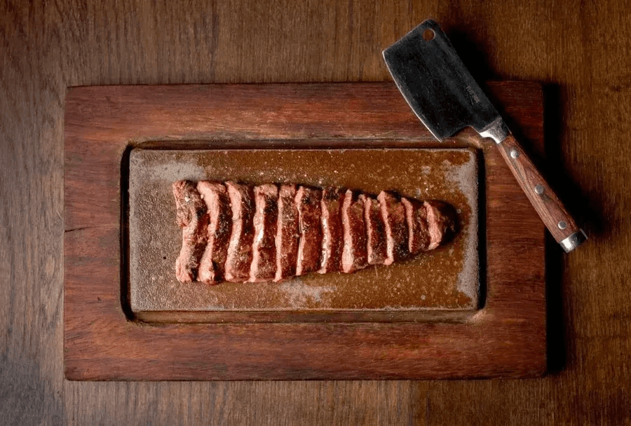 A wooden tray with a knife, some meat and dimly lit candle.