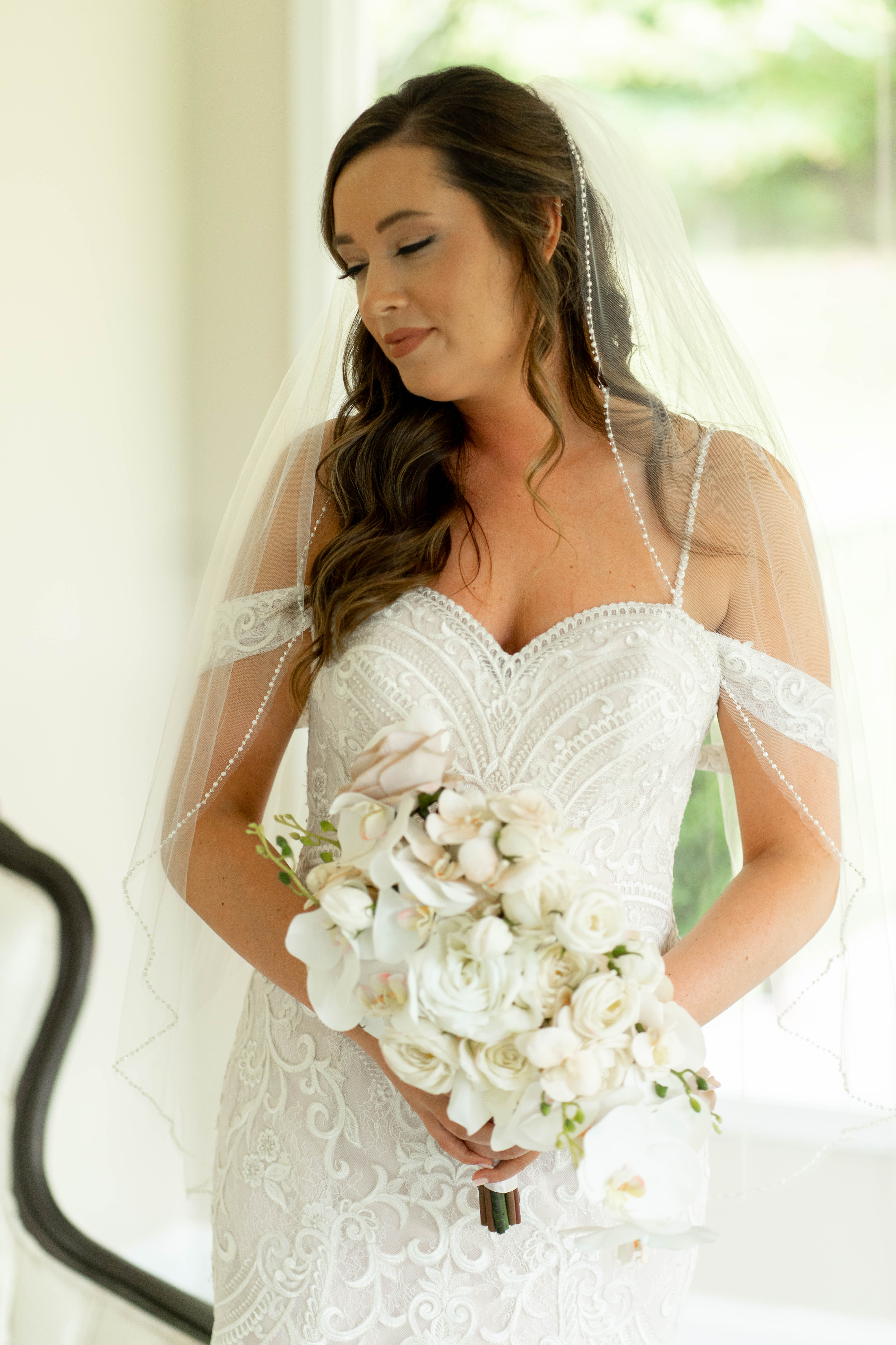 A couple in wedding attire walks hand in hand across a sunlit field.