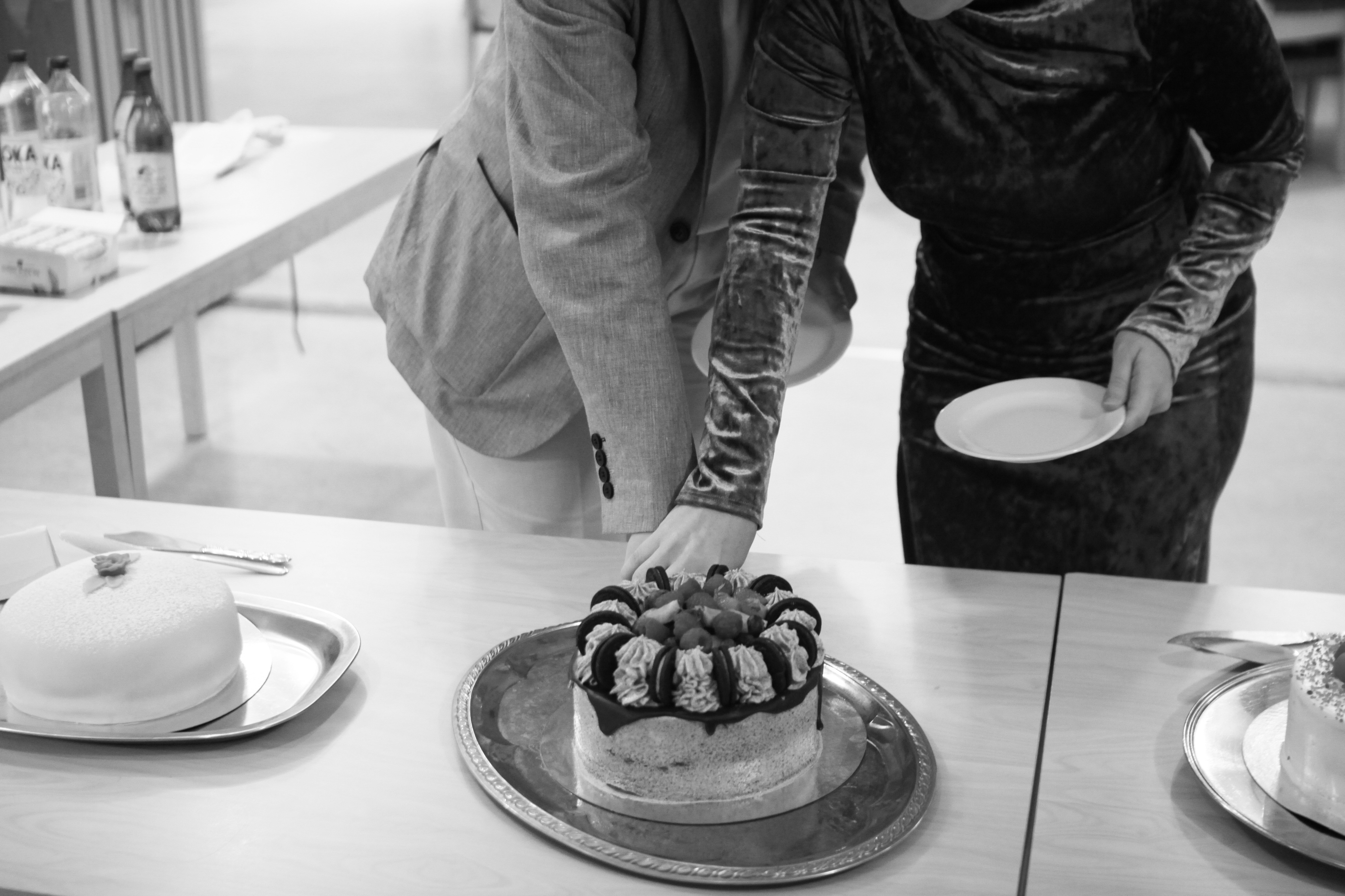 Two people holding a cake cutter and cutting a cake.