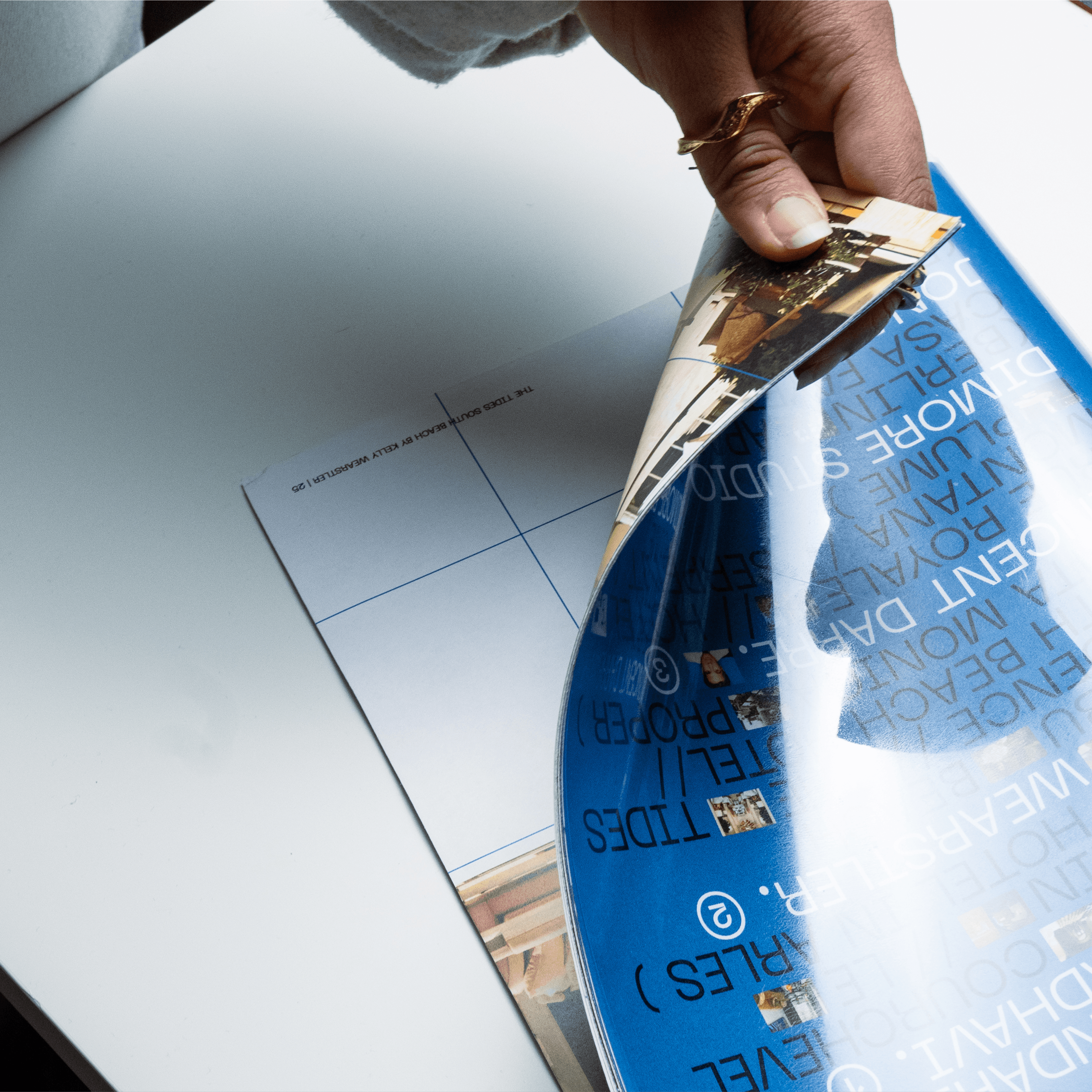 A person is flipping through a glossy magazine, showcasing a page with blue and white text and images featuring modern architecture and design elements.