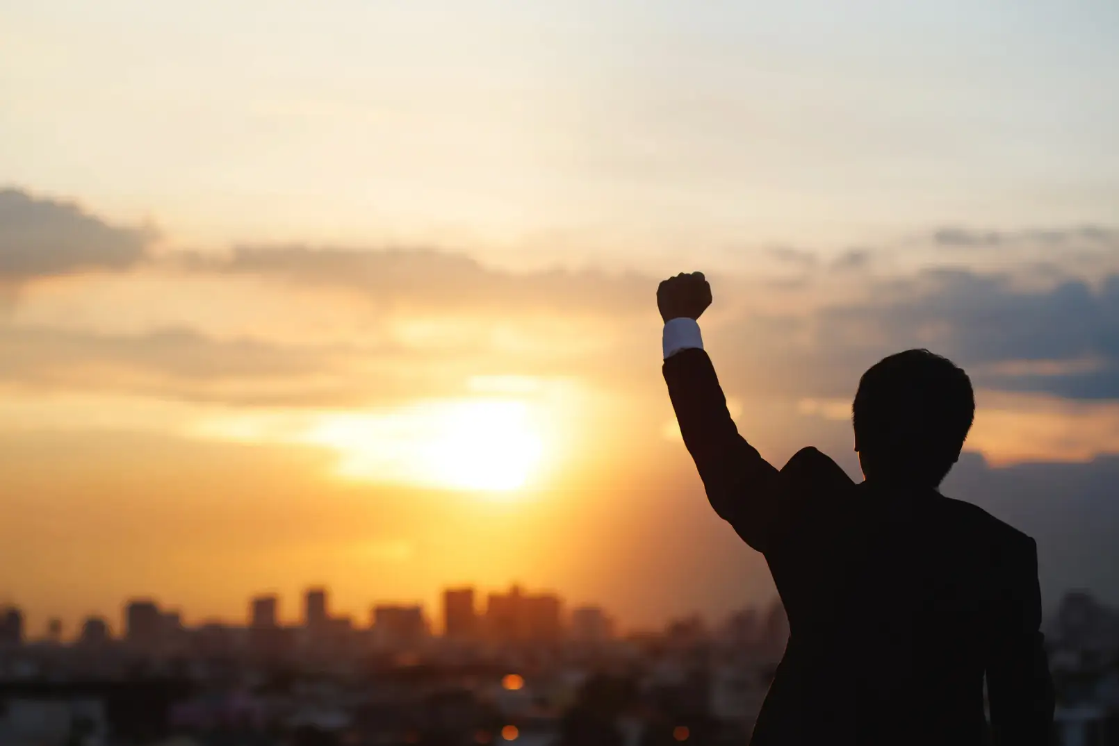 Silhouette einer Person mit erhobener Faust vor Sonnenaufgang als Symbol für Erfolg und Motivation