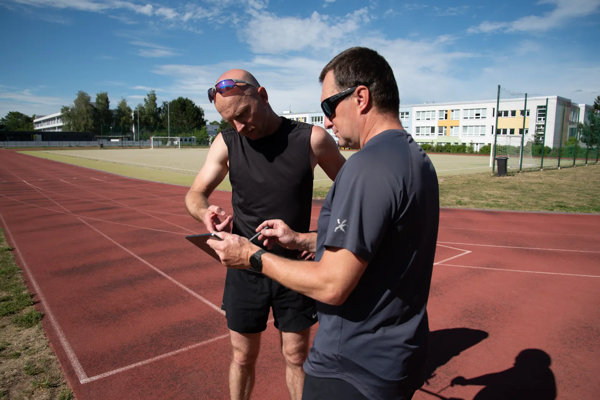 Trenér a běžec konzultují tréninková data na tabletu na atletické dráze