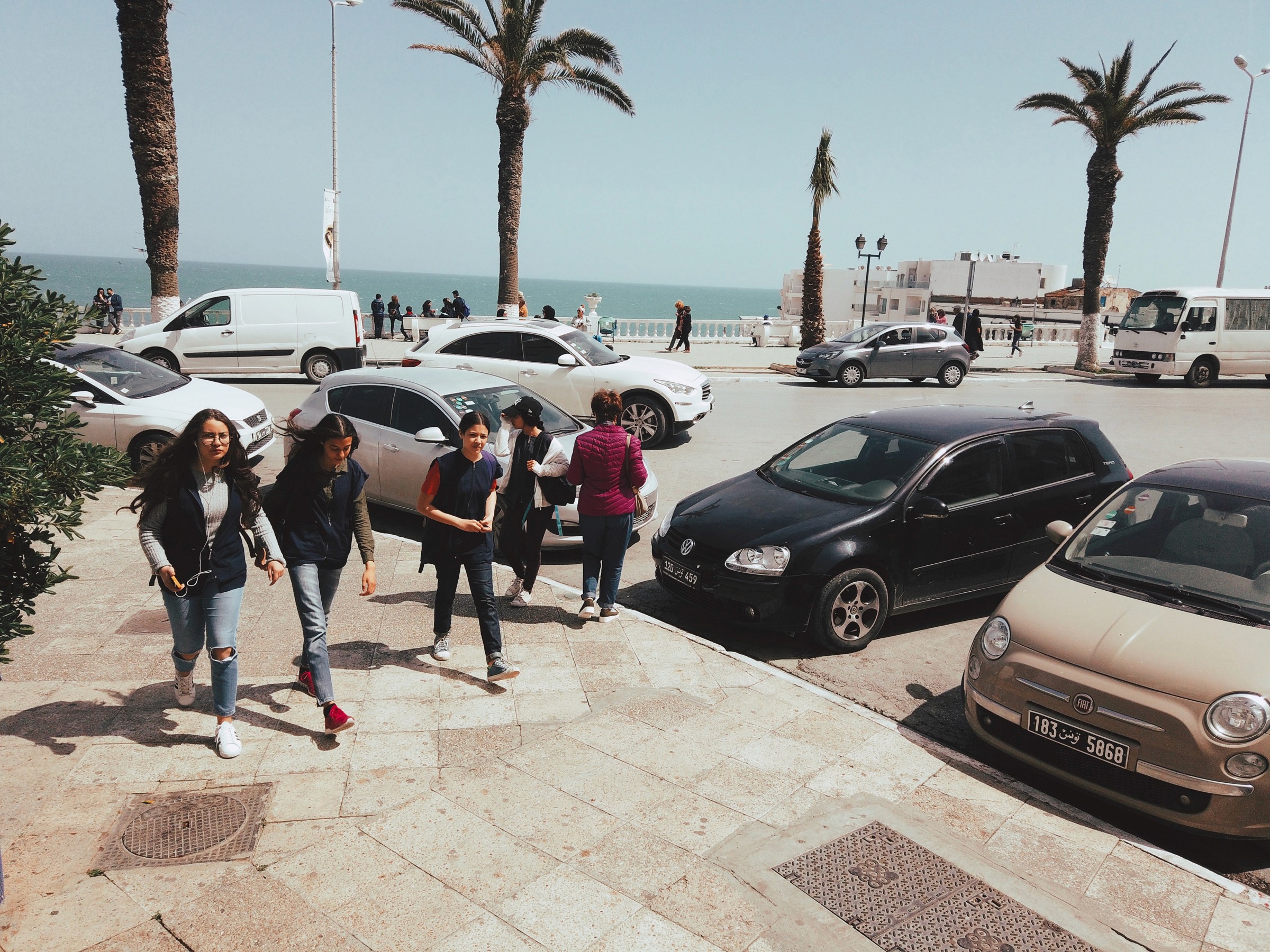 Un groupe de jeune filles tunisiennes se promenant au bord de la mer devant une rue où sont parquées des voitures