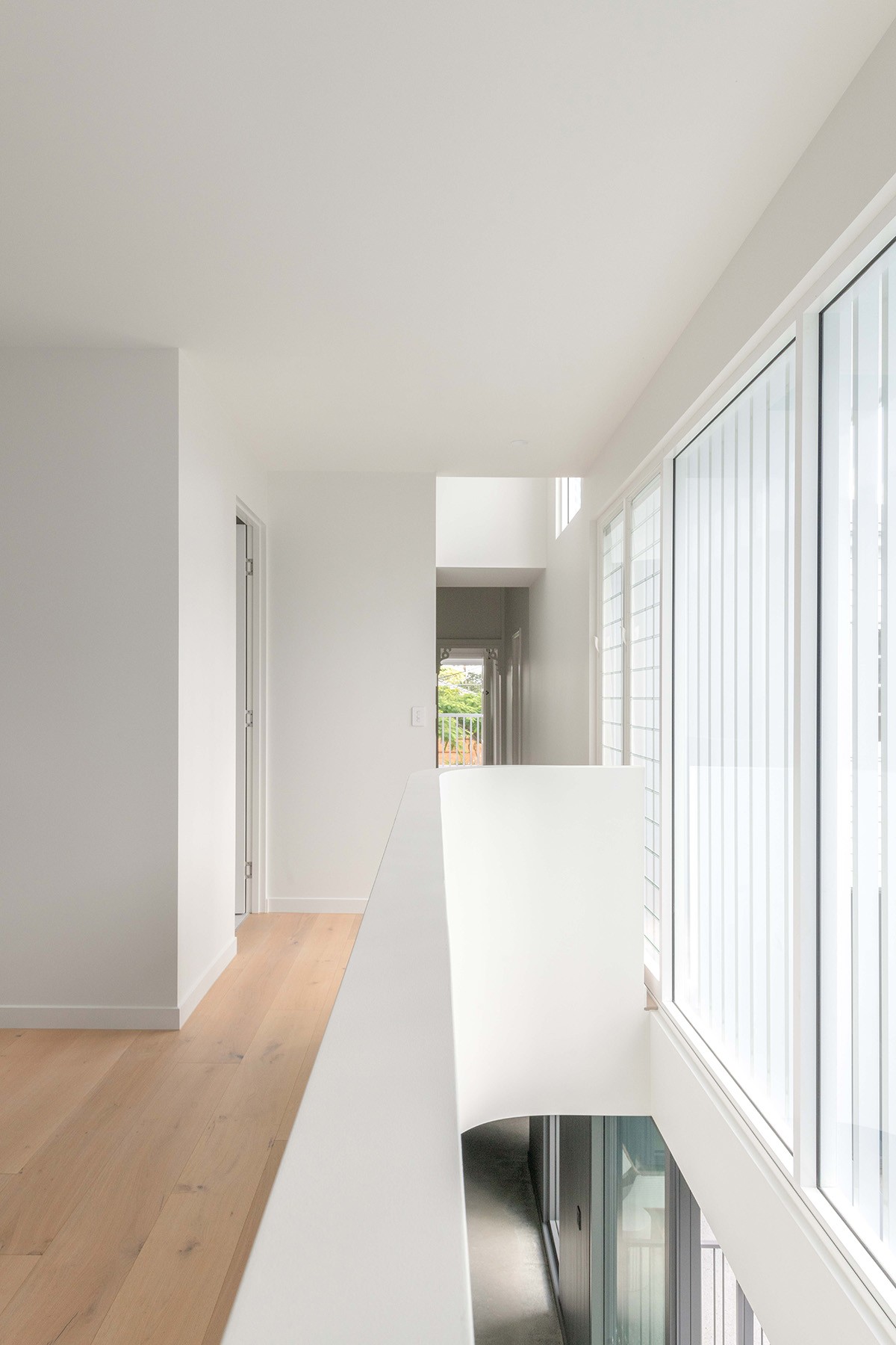 Upper-level circulation space at The Stables, with white balustrades, timber flooring, and full-height glazing bringing daylight into the interior.