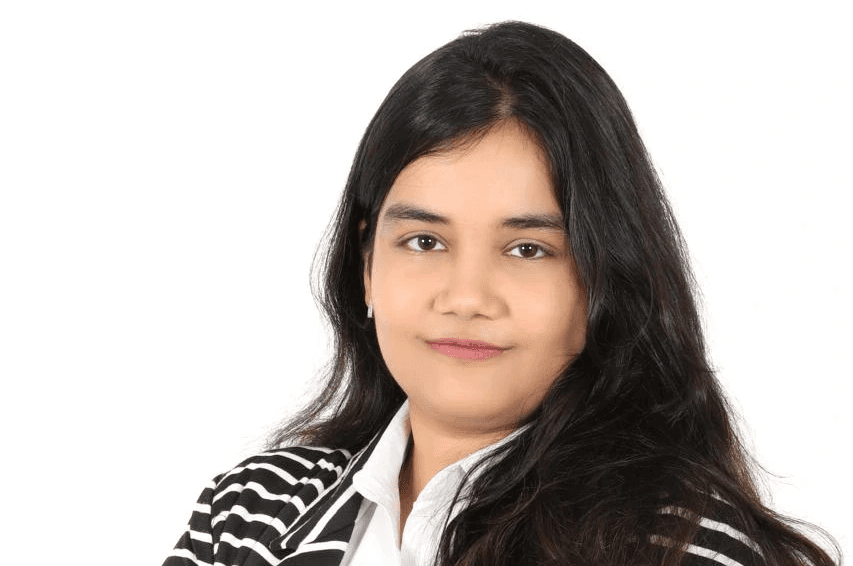 A woman with long black hair, wearing a striped blazer and a white shirt, smiles confidently at the camera.
