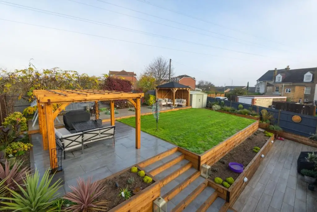 A panoramic view of a garden featuring green grass, seating areas, and surrounding residential buildings.