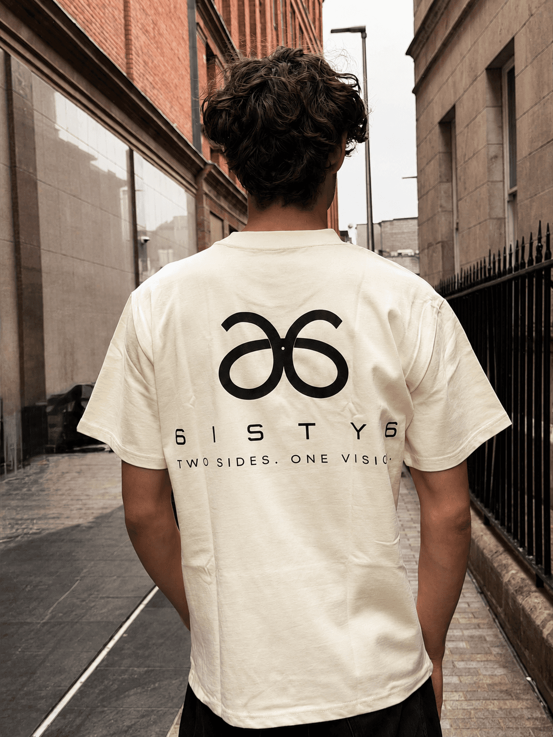 Back view of a cream 6ISTY6 Signature Tee with the Two Sides One Vision graphic