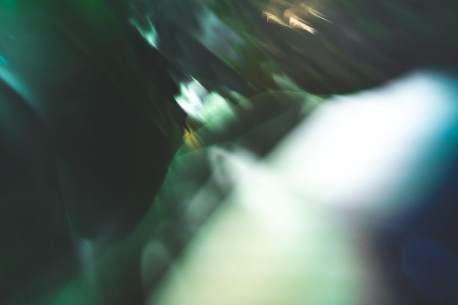 An abstract image with blurred shapes and colors, primarily featuring greens and soft light.