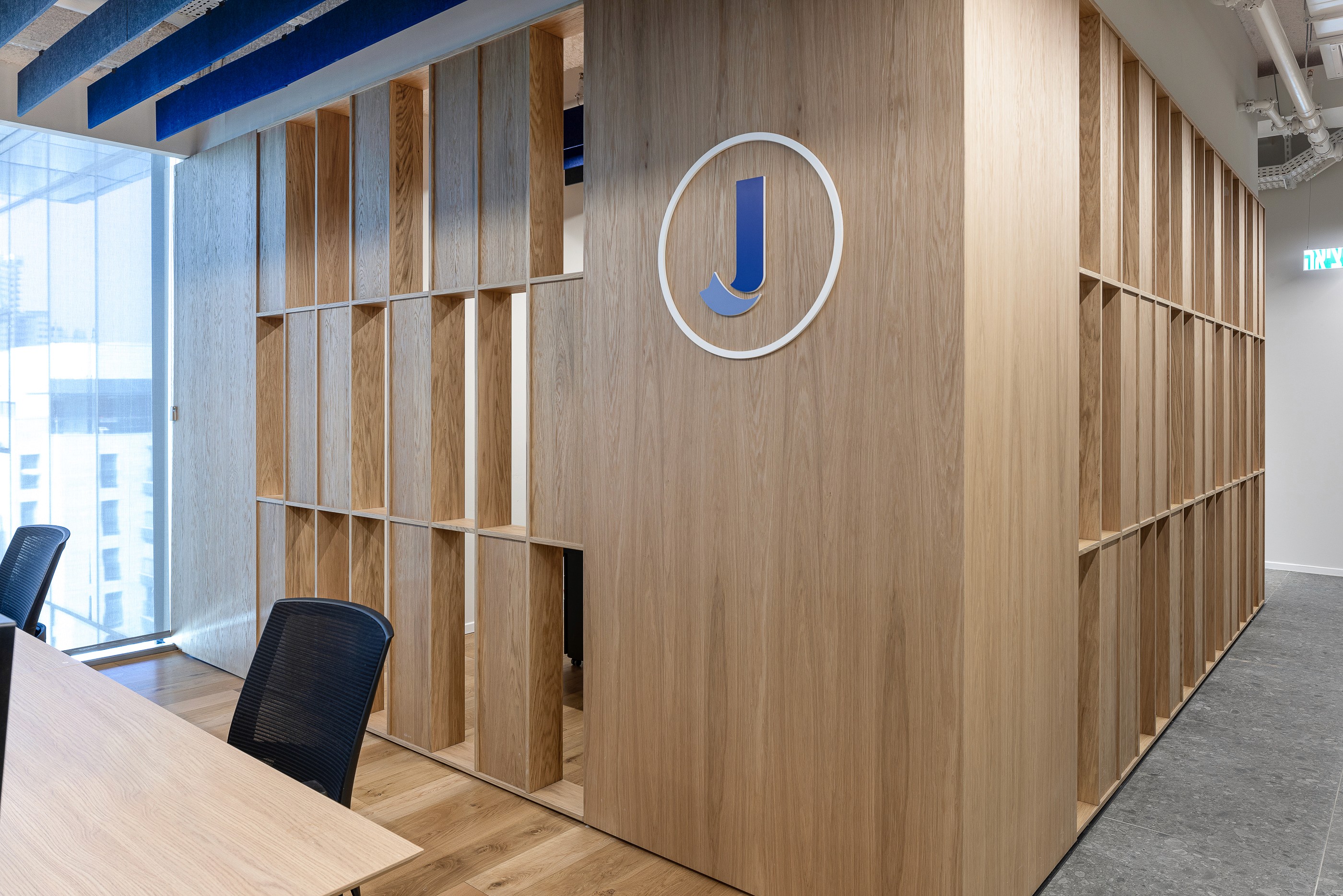 פרט אדריכלי: מחיצת רפפות עץ (Timber Slats) מרצפה לתקרה, המייצרת פרטיות חלקית ומשחקי אור וצל מעניינים לאורך המסדרון.