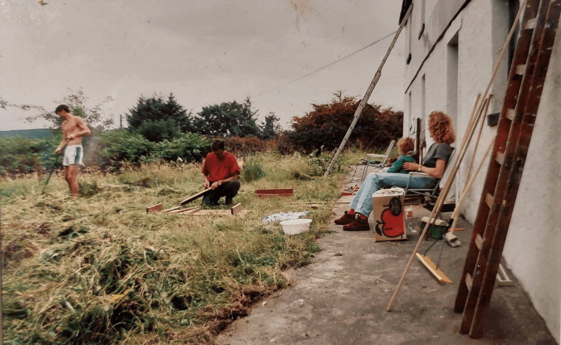 Old photo of the strawberryfield in 1997. Peter is working on the garden and Margaret is holding Yosta on her lap.