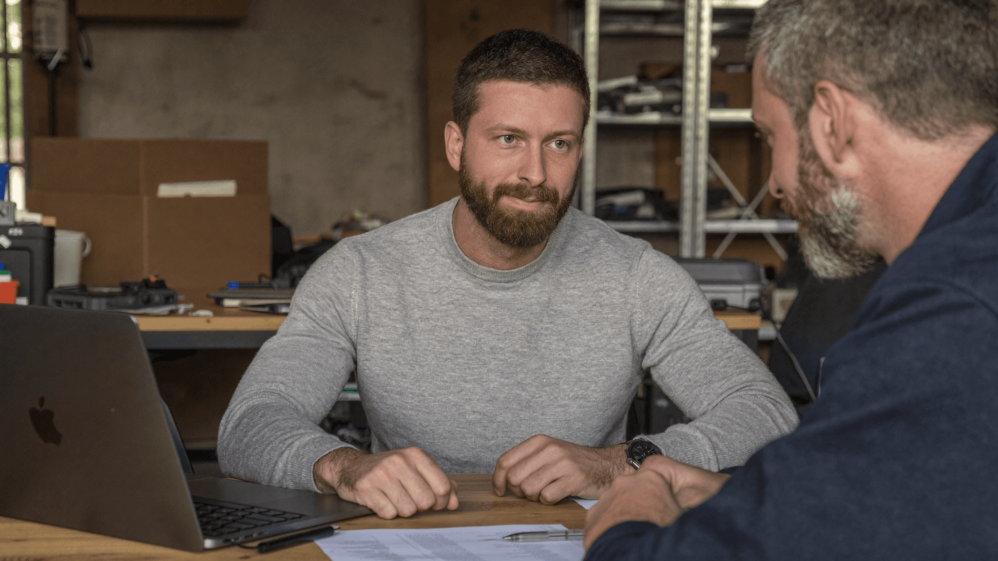 Geschäftstreffen in der Werkstatt. Zwei Männer diskutieren mit Laptop und Dokumenten.