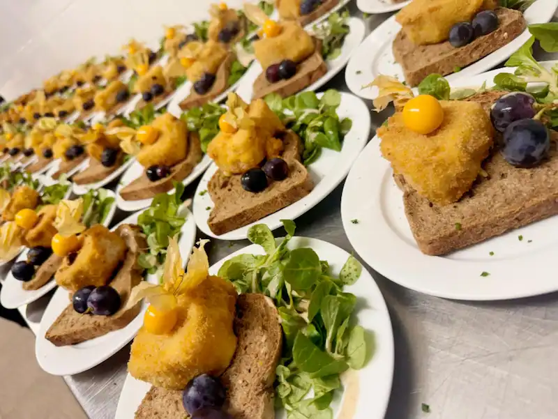 Modern indoor space with large glass doors, lush greenery, and a cozy seating area visible beyond.