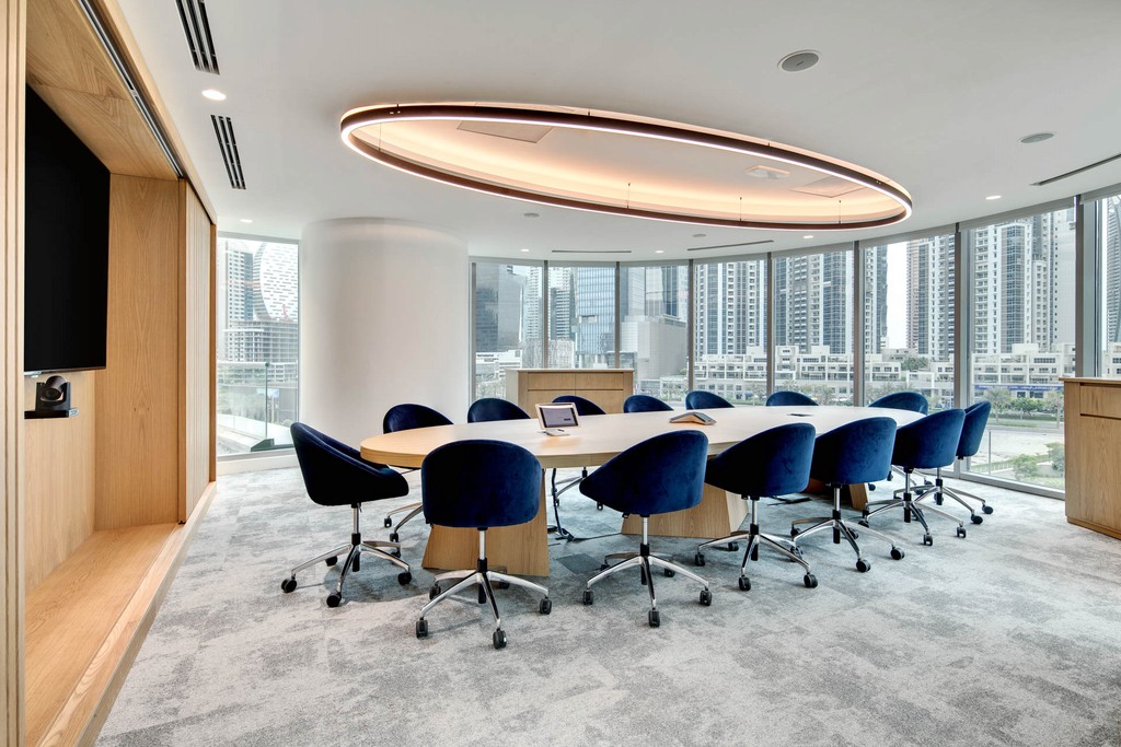 Conference room at The Binary by OMNIYAT, showcasing blue chairs and a prominent circular light overhead.