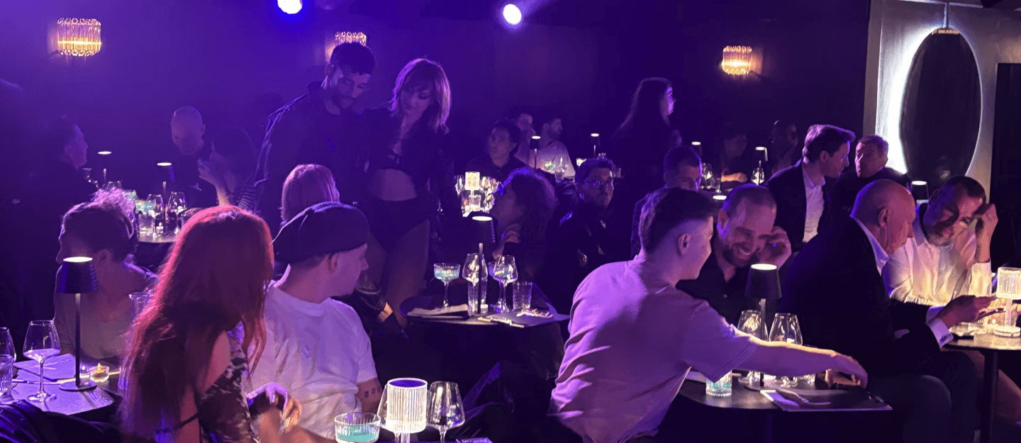 Guests smiling and conversing around intimate tables at Lou Diprey cabaret, bathed in warm purple lighting, capturing the lively post-show atmosphere