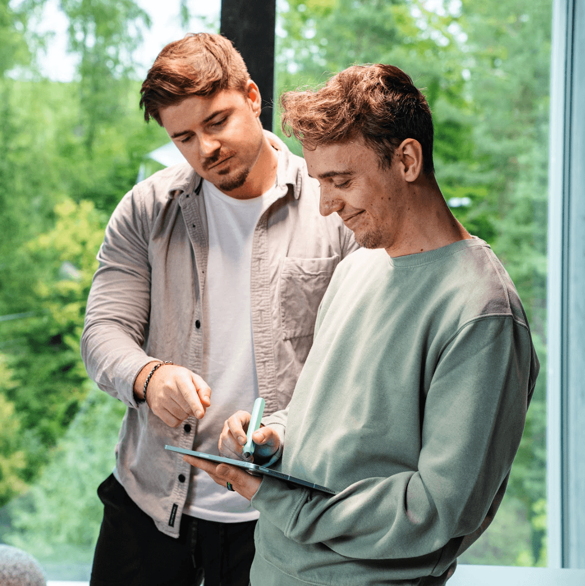 A young person with curly hair smiles at the camera while sitting in front of a laptop against a dark background.