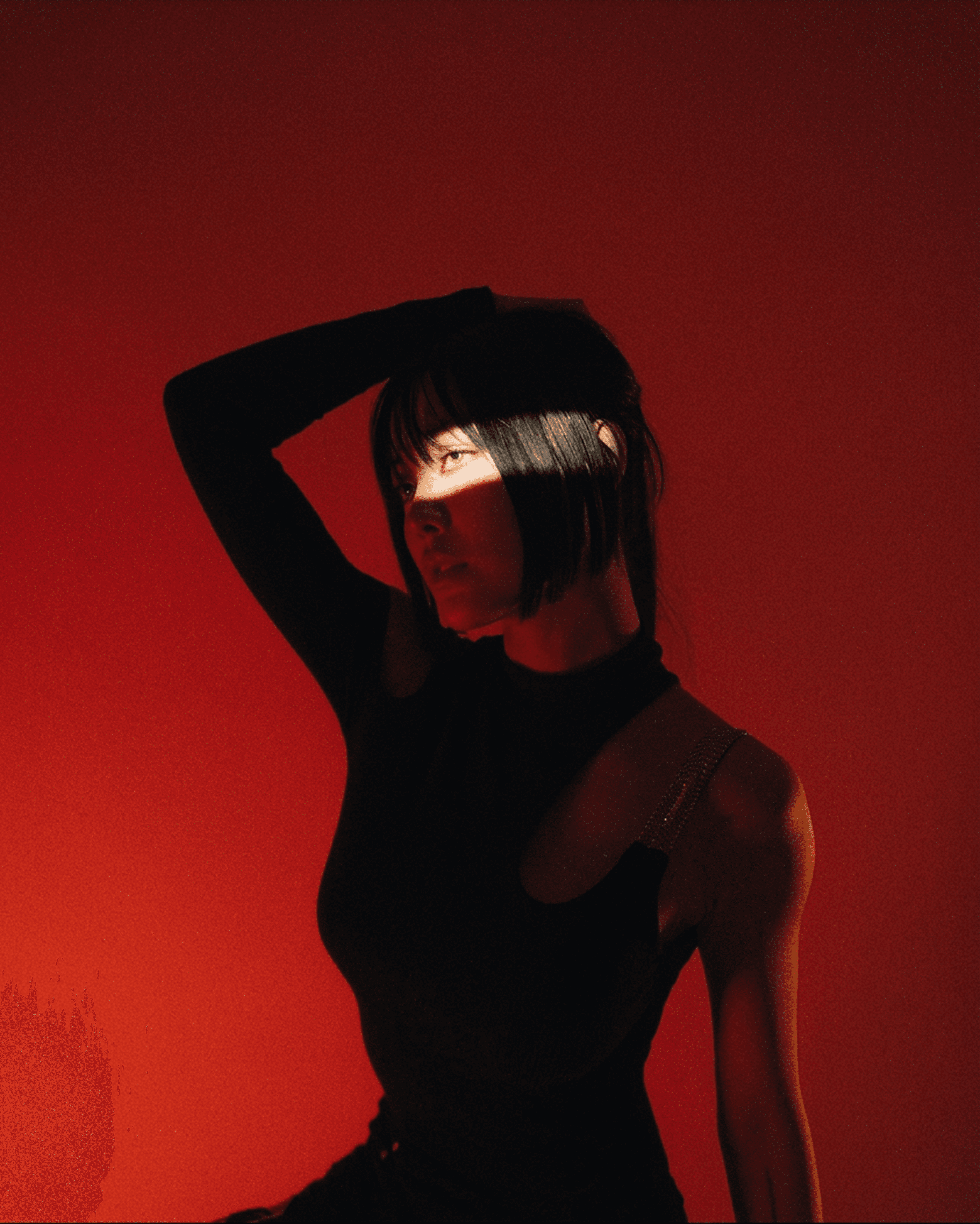 Woman with dark hair and bangs in black, dramatic red lighting and shadow.