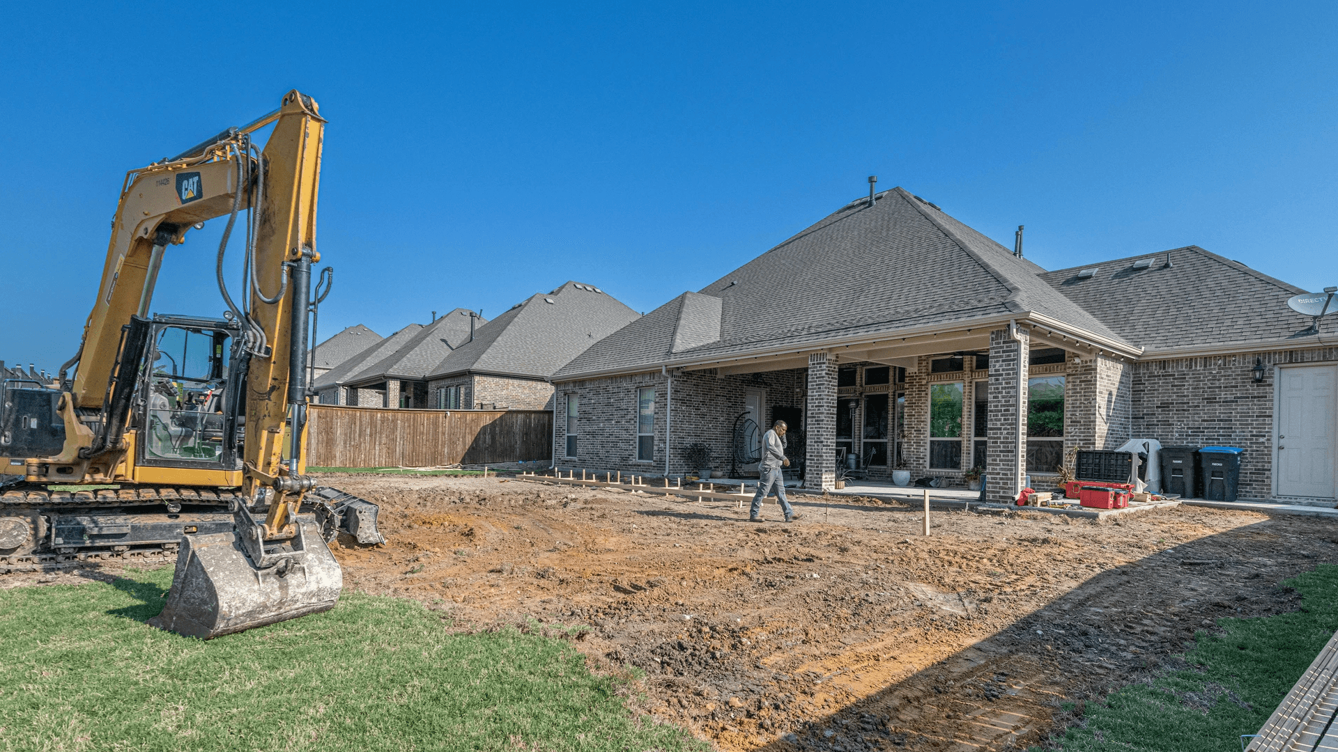 A large yellow excavator finishes construction on a residential home's foundation