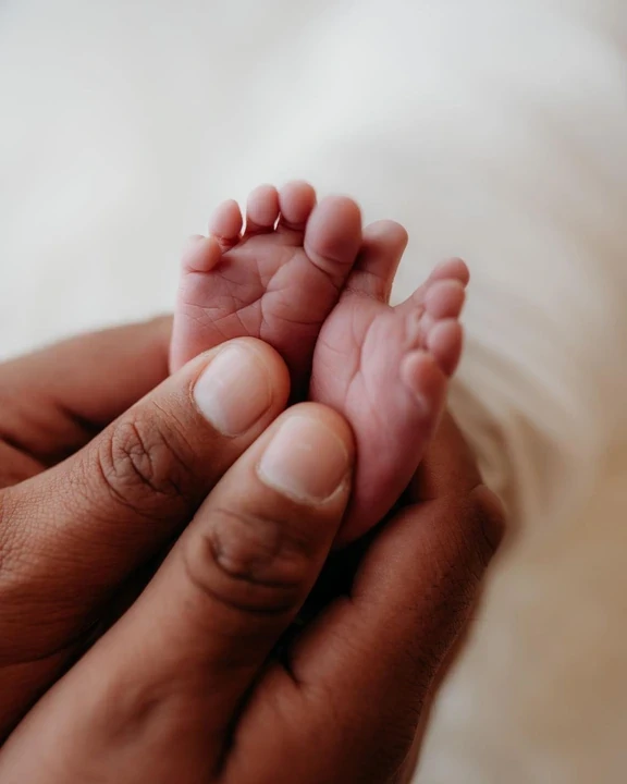 Tiny newborn feet gently supported by adult fingers