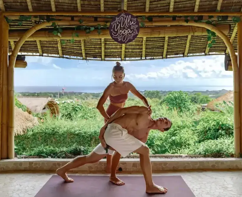 Instructor providing hands-on alignment adjustment to a student during yoga teacher training in the bamboo ocean-view shala.