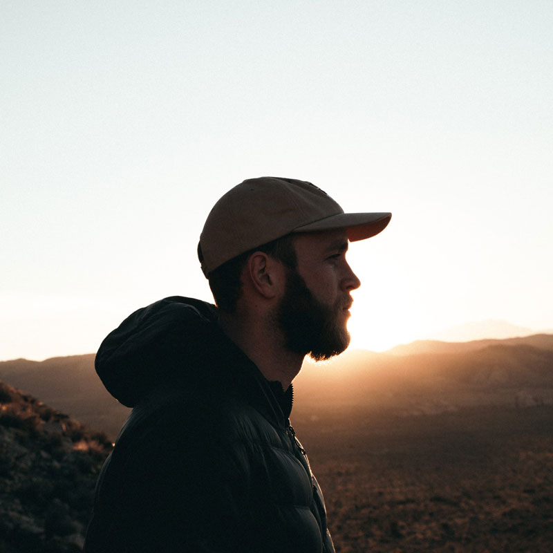 Side shot of a aman wearing a cap with the sun setting in the background