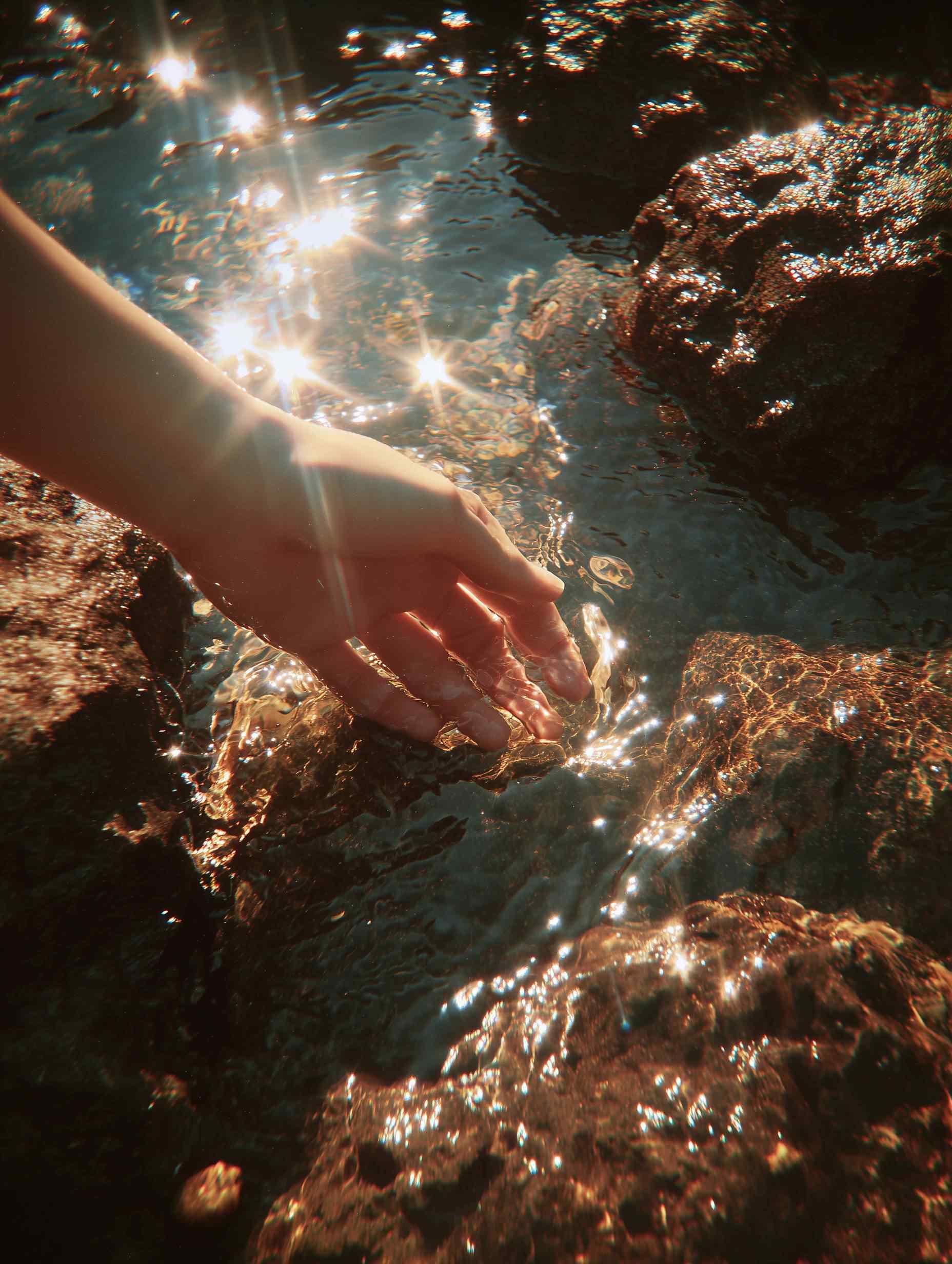 Hand immersed in radiant golden-lit water with rocks