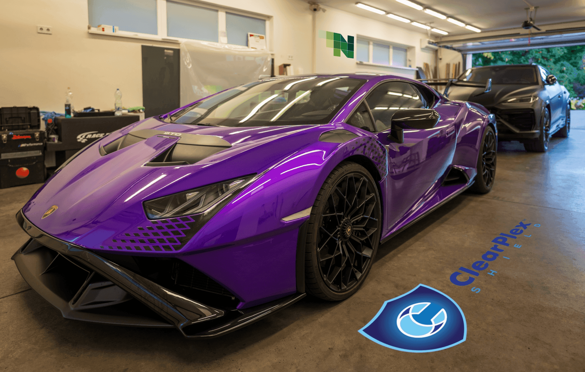 Extrém sportautók védelme: élénk lila Lamborghini Huracan STO vár ClearPlex szélvédővédő fóliázásra a Nortek budapesti stúdiójában, a háttérben egy matt fekete Lamborghini Urus modellel.