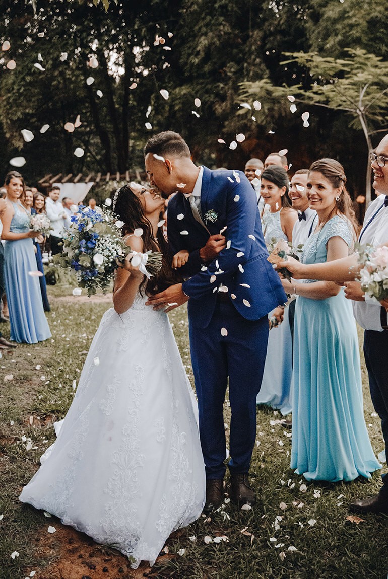 A bride and groom share a kiss surrounded by a joyful bridal party.