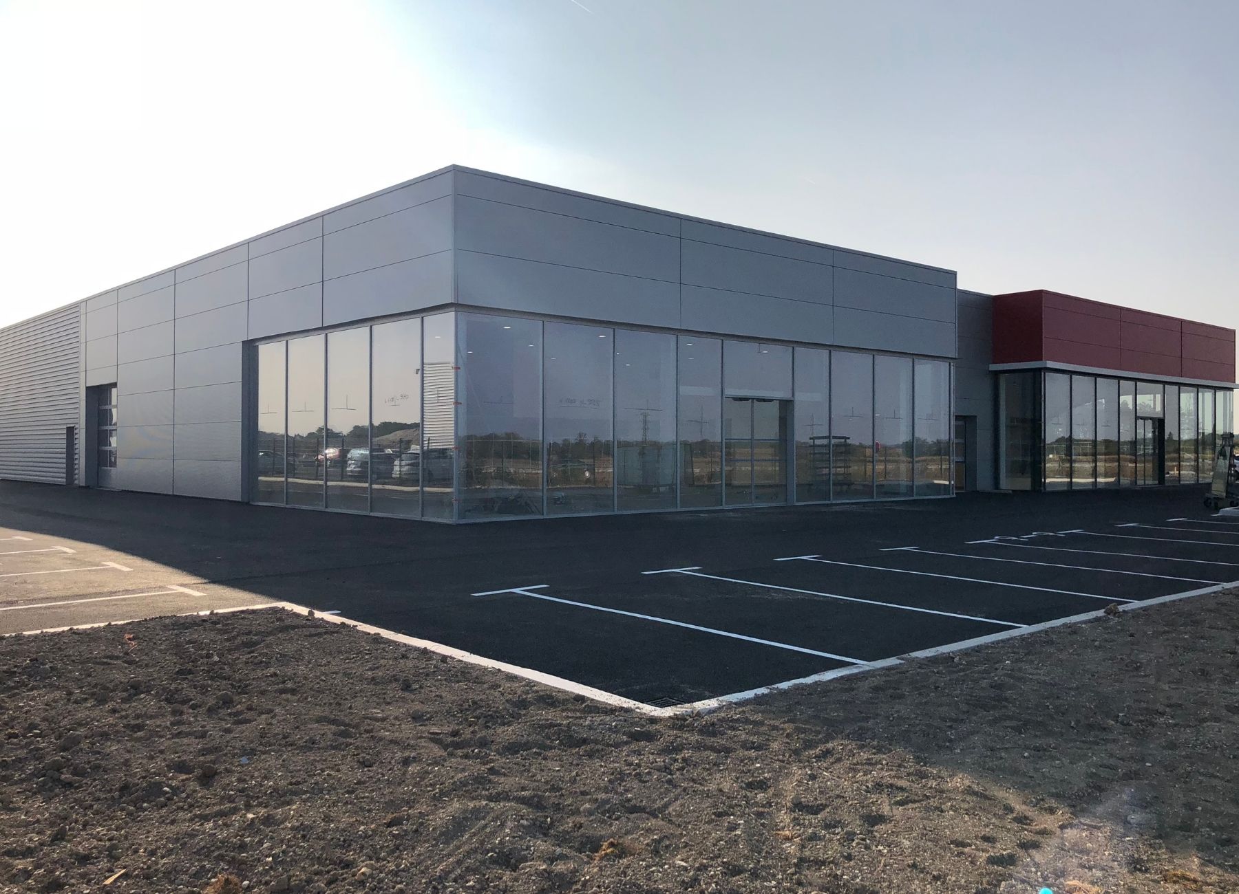 Bâtiment commercial terminé avec bardage métallique clair et parking aménagé.