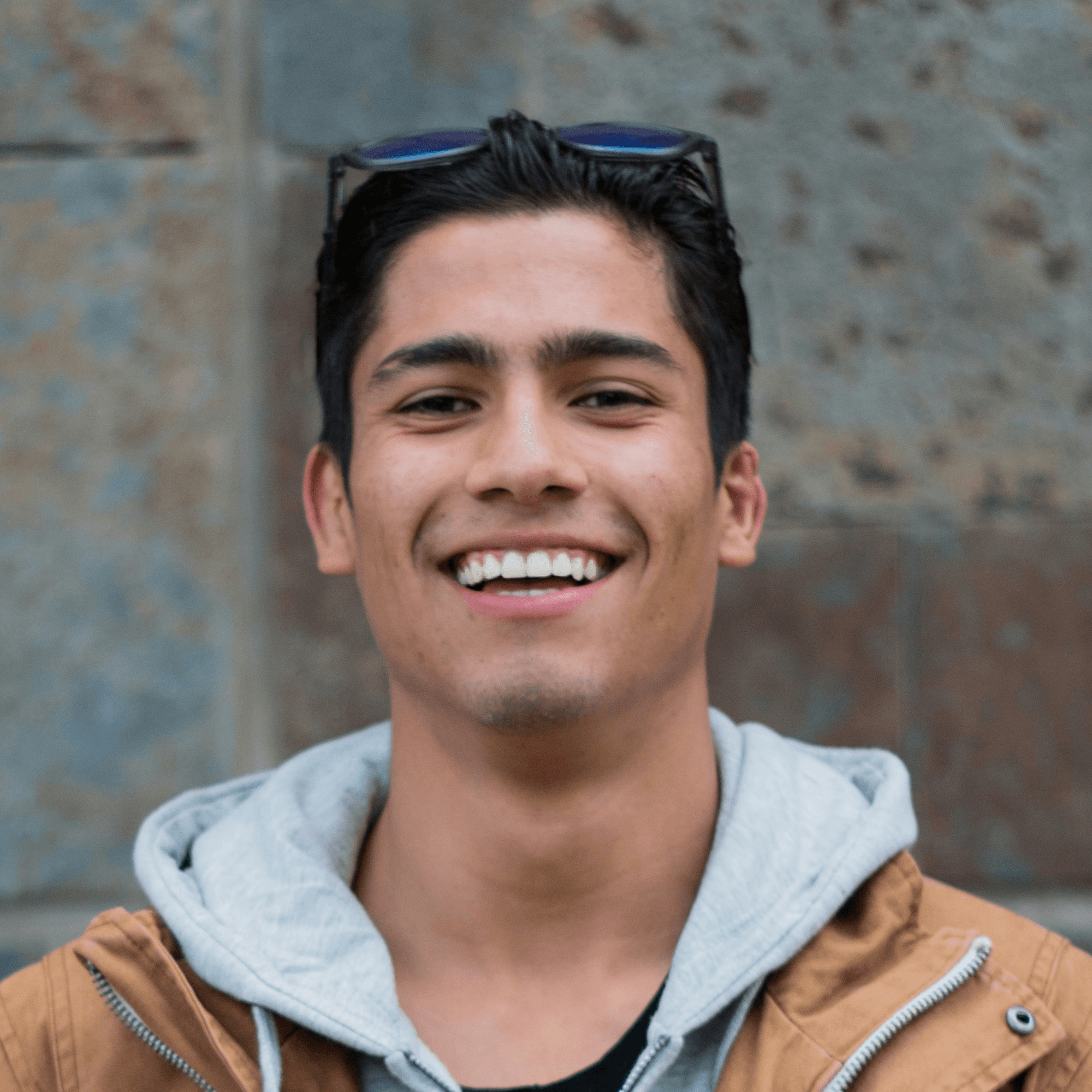 man in brown coat standing near concrete wall smiles