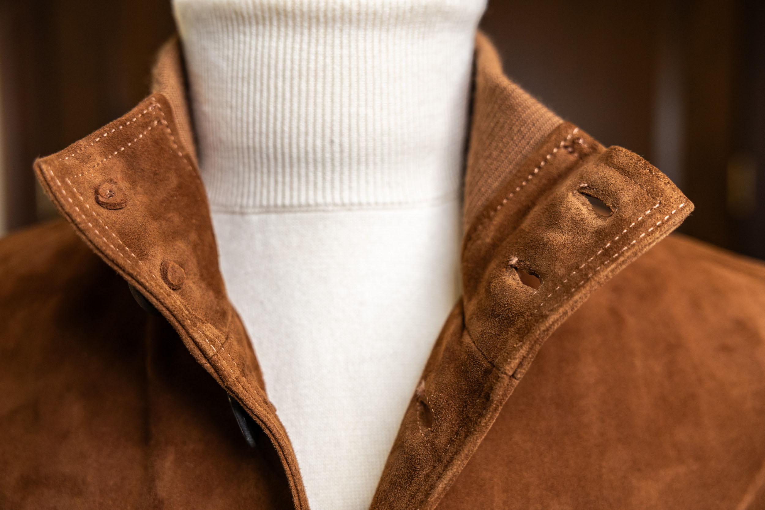 A close-up view of a Don Marrón suede jacket collar showcasing rich brown calf suede, refined stitching, and tailored craftsmanship styled over a cream turtleneck.
